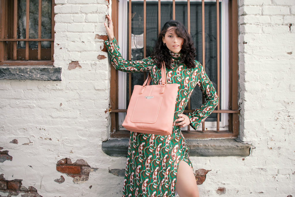 Top 5 Large Handbags for Women - Pictured here is a woman in a green dress leaning up against a brick wall with her large salmon Lexi Tote Bag.